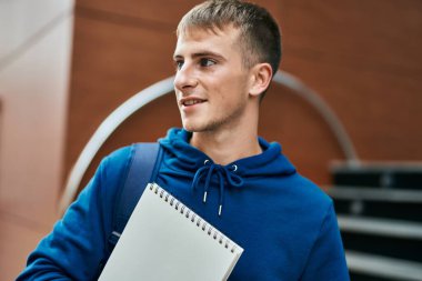 Üniversitede elinde defterle gülümseyen sarışın genç bir öğrenci..