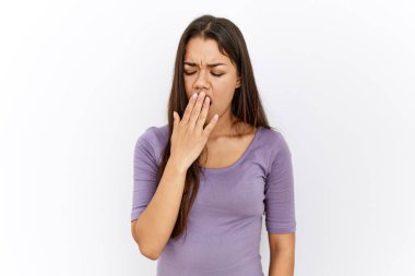 Genç esmer kadın izole edilmiş arka planda dikiliyor. Elle ağzını kapatmaktan sıkılmış. Huzursuz ve uykulu.. 