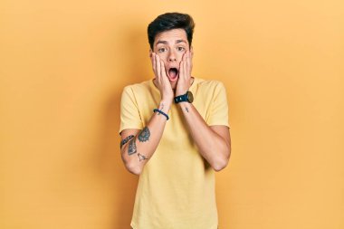 Latin asıllı genç bir adam günlük sarı tişört giyiyor. Korkmuş ve şok olmuş. Şaşırmış ve şaşırmış bir halde. 