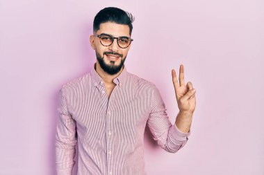 Sakallı, sıradan tişörtlü ve gözlüklü, gülümseyen, kameraya göz kırpan ve zafer işareti yapan yakışıklı bir adam. İki numara.. 