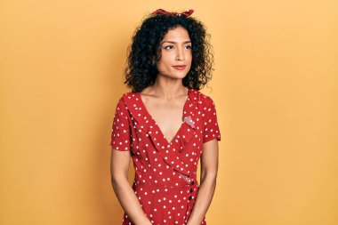 Yazlık elbise giyen genç Latin kız gülümsüyor, yan tarafa bakıyor ve düşünüyor.. 