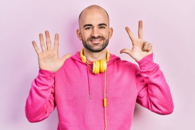 Spor kıyafetleri giyen ve kulaklık takan genç kel adam 8 numaralı parmaklarını gösterip işaret ederken kendinden emin ve mutlu bir şekilde gülümsüyor.. 