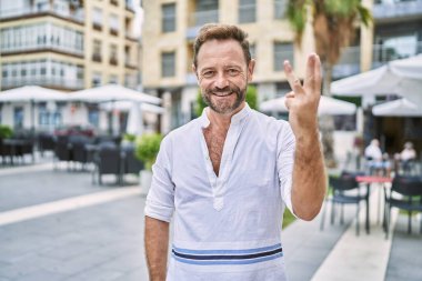 Şehirdeki orta yaşlı adam üç numaralı parmaklarını gösterip onu işaret ederken kendinden emin ve mutlu gülümsüyor.. 