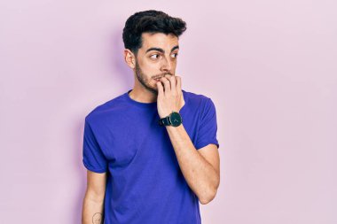 Günlük tişört giyen genç İspanyol adam gergin ve gergin görünüyor. Ağzı tırnak yiyen ellerle. anksiyete. 