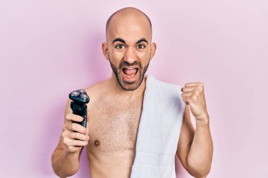 Genç kel adam elinde elektrikli jilet tutarken gururla bağırıyor zaferi ve başarıyı kutluyor. Kollarını kaldırarak heyecanlanıyor. 