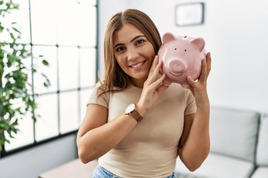 Genç İspanyol kadın gülümsüyor. Kumbarasını evinde tutuyor.