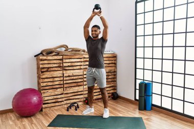 Genç Arap adam gülümsüyor spor merkezinde kettlebell ile antrenman yapıyor.