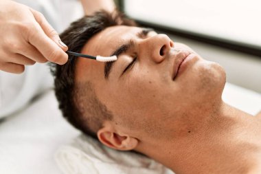 Young hispanic man relaxed having eyebrows treatment at beauty center