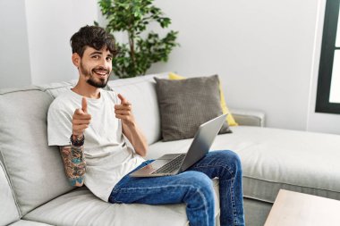 Kanepede oturan sakallı İspanyol adam mutlu ve komik yüzüyle kamerayı işaret ediyor. iyi enerji ve titreşimler. 