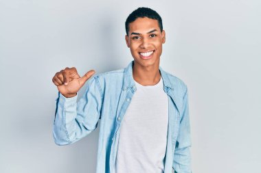 Genç, Afro-Amerikalı, günlük kıyafetler giymiş, bir numaralı parmağını gösterip, gülümseyen, kendinden emin ve mutlu.. 