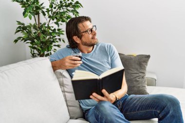 Orta yaşlı beyaz bir adam kitap okuyor evde şarap içiyor.