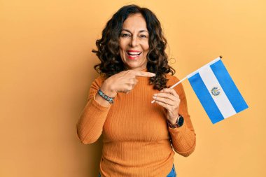 El Salvador bayrağını tutan orta yaşlı İspanyol kadın mutlu bir şekilde el ve parmağıyla işaret ediyor. 