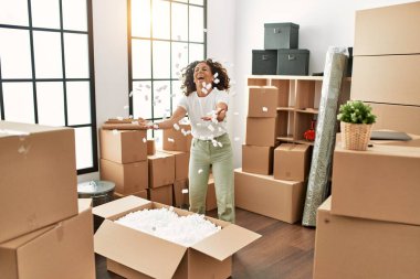 Orta yaşlı İspanyol kadın yeni evinde kutuları açarken gülümsüyor.