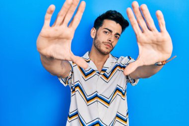 Gündelik kıyafetler giyen, el ve parmaklarını kullanarak çerçeve yapan genç İspanyol adam, kamera açısı. 