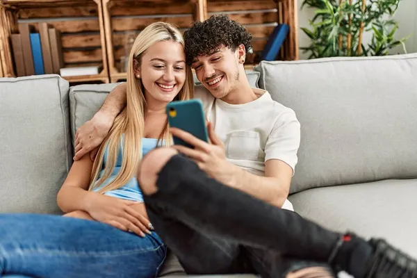 自宅のソファに座っているスマートフォンを使用して若いカップル — ストック写真