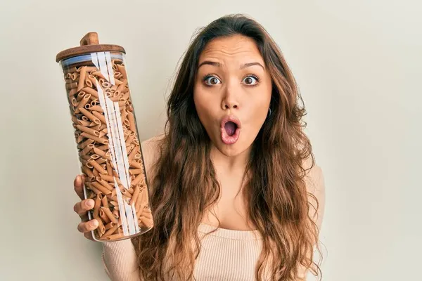 Joven Chica Hispana Sosteniendo Tarro Con Pasta Macarrones Asustada Sorprendida — Foto de Stock