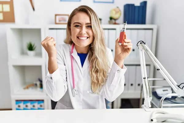 Young Beautiful Doctor Woman Holding Electronic Cigarette Clinic Screaming Proud — Stock Photo, Image