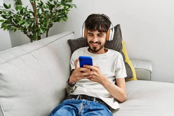 Jovem Hispânico Usando Smartphone Fones Ouvido Deitados Sofá Casa — Fotografia de Stock