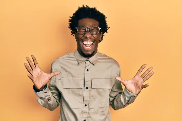 若いアフリカ系アメリカ人の男性は 腕を上げ 興奮して叫んで目を閉じて成功のために狂気と狂気を祝うカジュアルな服や眼鏡を着用 勝者のコンセプト — ストック写真