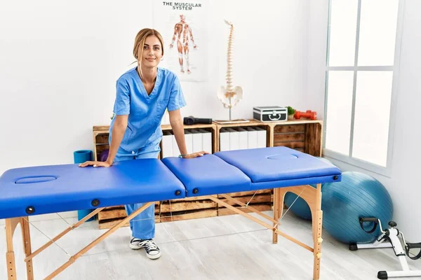 Junger Kaukasischer Physiotherapeut Lächelt Glücklich Auf Tisch Der Klinik Gelehnt — Stockfoto