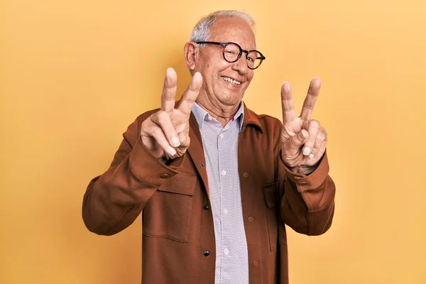 Starszy Mężczyzna Siwych Włosach Luźnej Kurtce Okularach Uśmiechnięty Kamery Pokazujący — Zdjęcie stockowe