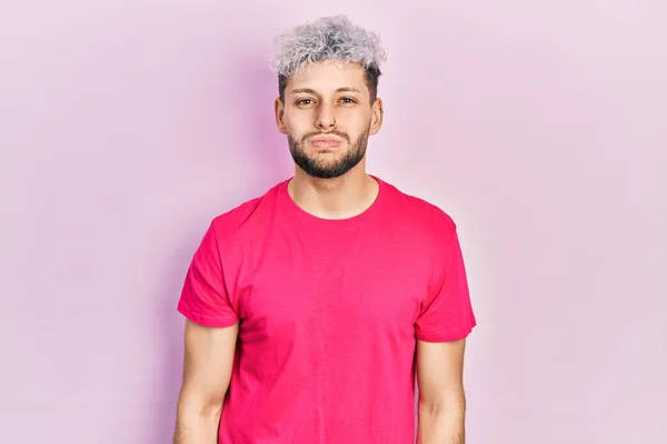 Young hispanic man with modern dyed hair wearing casual pink t shirt puffing cheeks with funny face. mouth inflated with air, crazy expression.