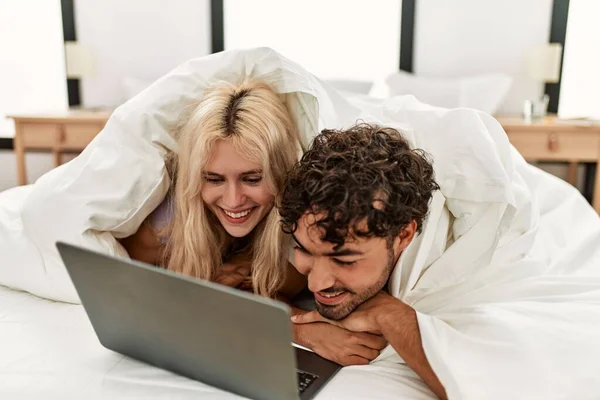 年轻漂亮的夫妇在床上看着铺满床单的电影 — 图库照片