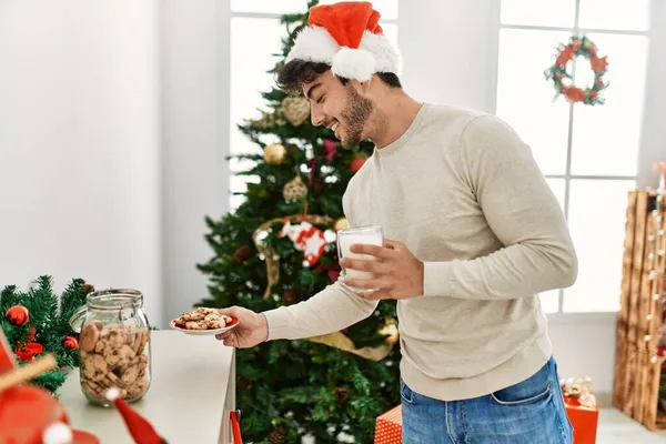 Jovem Hispânico Vestindo Chapéu Natal Segurando Biscoitos Leite Casa — Fotografia de Stock