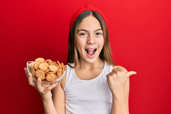 Beautiful Brunette Little Girl Holding Salty Biscuits Bowl Pointing Thumb — ストック写真