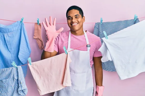 Joven Hombre Hispano Guapo Usando Delantal Más Limpio Sosteniendo Ropa —  Fotos de Stock