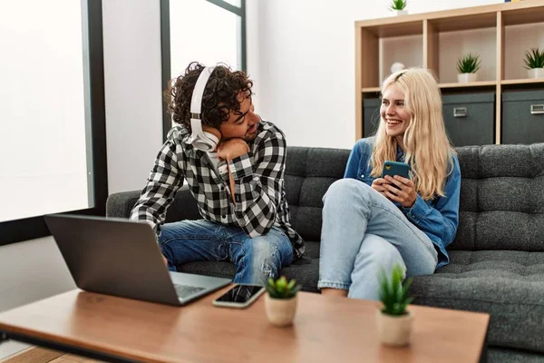 Evde dizüstü bilgisayar ve akıllı telefon kullanan genç çift mutlu..