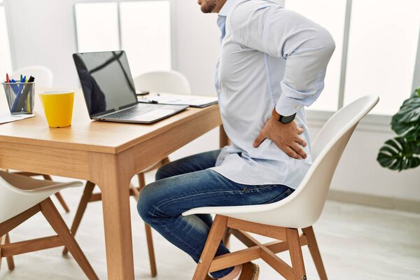 Young hispanic businessman working at the office. Sitting on the table with backache.