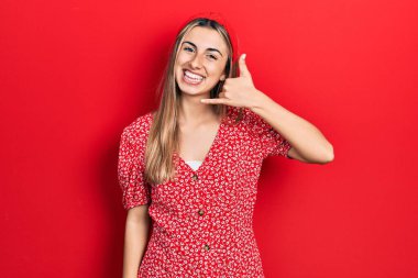 Yazlık elbise giymiş, gülümseyen, el ve parmaklarıyla telefon hareketi yapan, telefonda konuşan güzel İspanyol bir kadın. iletişim kavramları. 