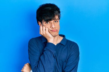 Yakışıklı hippi genç adam mavi arka planda mahsur kalmış, yorgun ve bunalımda kollarını kavuşturmaktan sıkılmış görünüyor.. 