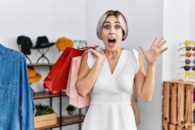 Mağazada alışveriş torbaları tutan genç ve güzel bir kadın zaferi mutlu bir gülümsemeyle ve ellerini kaldırarak kutluyor. 