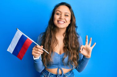 Rus bayrağı tutan genç İspanyol kız parmaklarıyla imza atıyor, gülümseyerek mükemmel bir sembol oluşturuyor. 