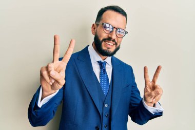 Sakallı, takım elbiseli ve kravatlı genç adam kameraya bakıp zafer işareti yapıyor. İki numara.. 