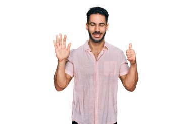 Hispanic man with beard wearing casual shirt showing and pointing up with fingers number six while smiling confident and happy. 