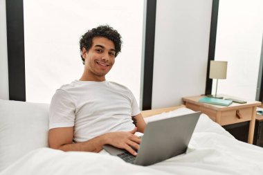 Genç İspanyol adam yatak odasında dizüstü bilgisayar kullanıyor..