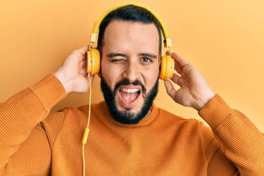 Sakallı genç adam müzik dinliyor kulaklık takıyor kameraya seksi bir ifadeyle bakıyor, neşeli ve mutlu bir yüzle.. 