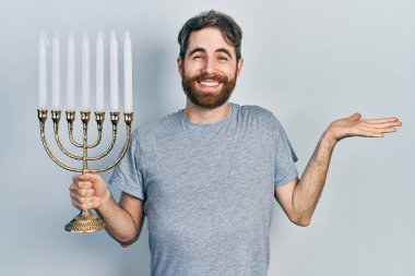 Sakallı, beyaz bir adam menorah Hanuka mumunu tutuyor. Başarımızı mutlu bir gülümsemeyle kutluyor. 