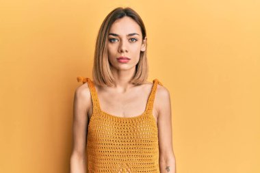 Sıradan sarı tişört giyen beyaz, genç bir kadın yüzünde ciddi bir ifadeyle rahatlamış. Basit ve doğal bir şekilde kameraya bakıyorsun.. 