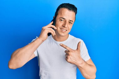 Yakışıklı genç adam akıllı telefondan konuşuyor. Gülümsüyor. Elinle ve parmağınla işaret ederek mutlu ol. 