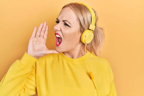 ヘッドフォンの叫びを使用して音楽を聞いている若いブロンドの女性は 口の中で手で大声で叫んでいます コミュニケーションの概念 — ストック写真