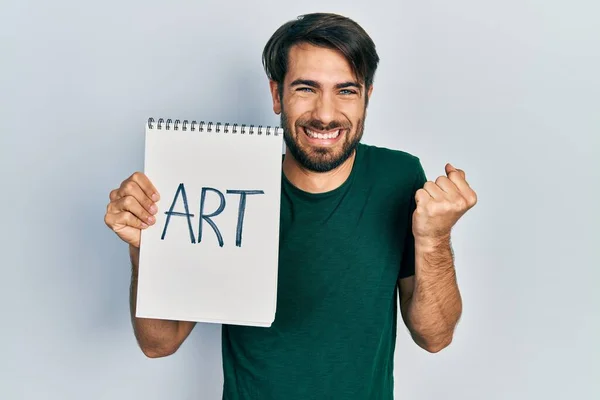 Joven Hispano Sosteniendo Cuaderno Arte Gritando Orgulloso Celebrando Victoria Éxito —  Fotos de Stock