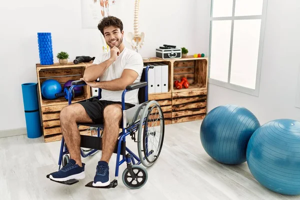 Hispanic Man Sitting Wheelchair Physiotherapy Clinic Looking Confident Camera Smiling — Stok fotoğraf