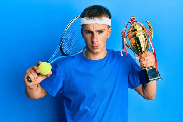 若い白人男性がトロフィーを持っているテニスをプレイ懐疑的で緊張 問題のために動揺を眉をひそめて 否定的な人 — ストック写真