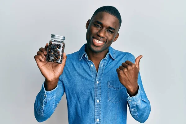 Joven Hombre Afroamericano Sosteniendo Frasco Con Granos Café Apuntando Pulgar — Foto de Stock