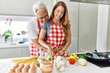 Orta yaşlı İspanyol çift mutlu bir şekilde gülümsüyor ve mutfakta yemek pişiriyor..