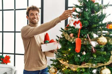 Genç İspanyol adam gülümsüyor. Evde kendine güvenen bir Noel ağacı süslüyordu.